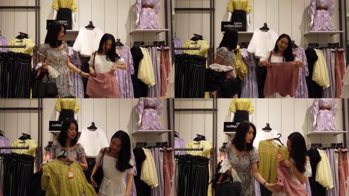 2位年轻的亚洲华裔女性朋友在购物中心的精品店购物，选择新衣服