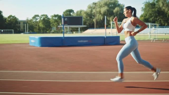 穿着浅蓝色运动上衣和打底裤的美丽健身女子在体育场慢跑。在一个温暖的夏日下午，她跑得很快。运动员在做她