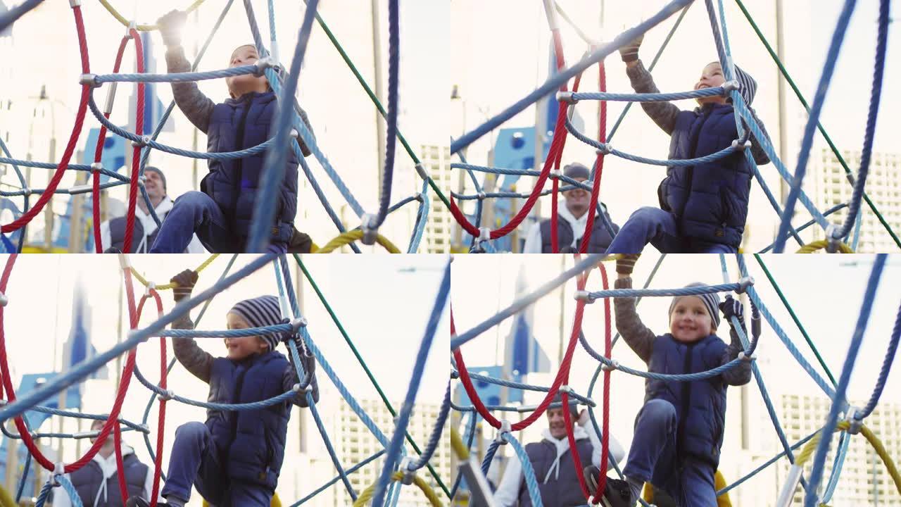 快乐的高加索男孩在操场上爬网结构
