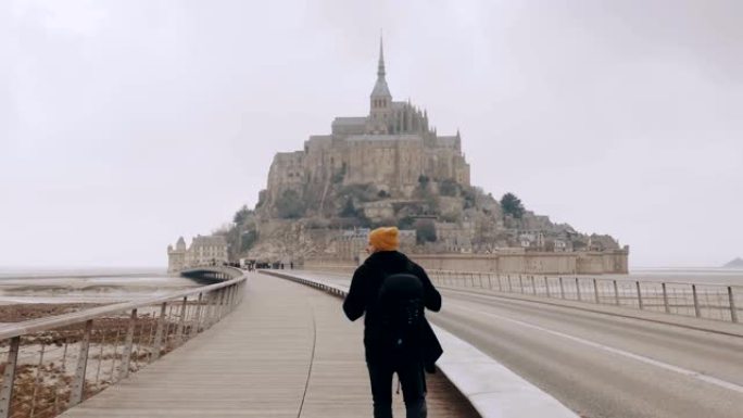 摄像机跟随快乐兴奋的游客背着背包步行到诺曼底的史诗圣米歇尔城堡慢动作。