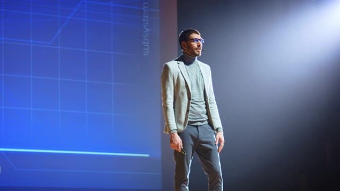 在舞台上，有远见的男性演讲者展示了新技术，使用遥控器进行演示，在屏幕上显示信息图表，统计动画。现场活