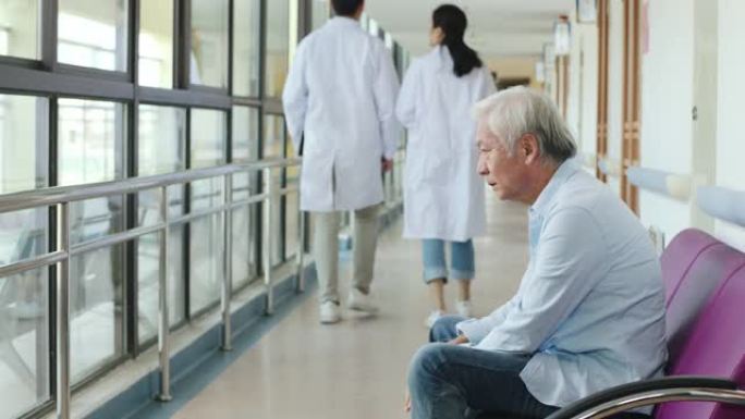 坐在医院走廊上的亚洲高级男子看上去很悲伤和沮丧