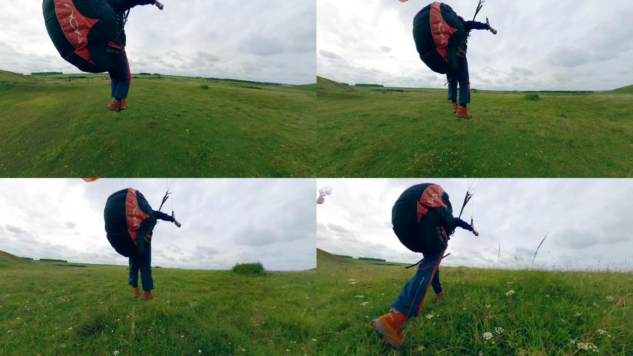 人驾驶滑翔伞，降落在草地上。