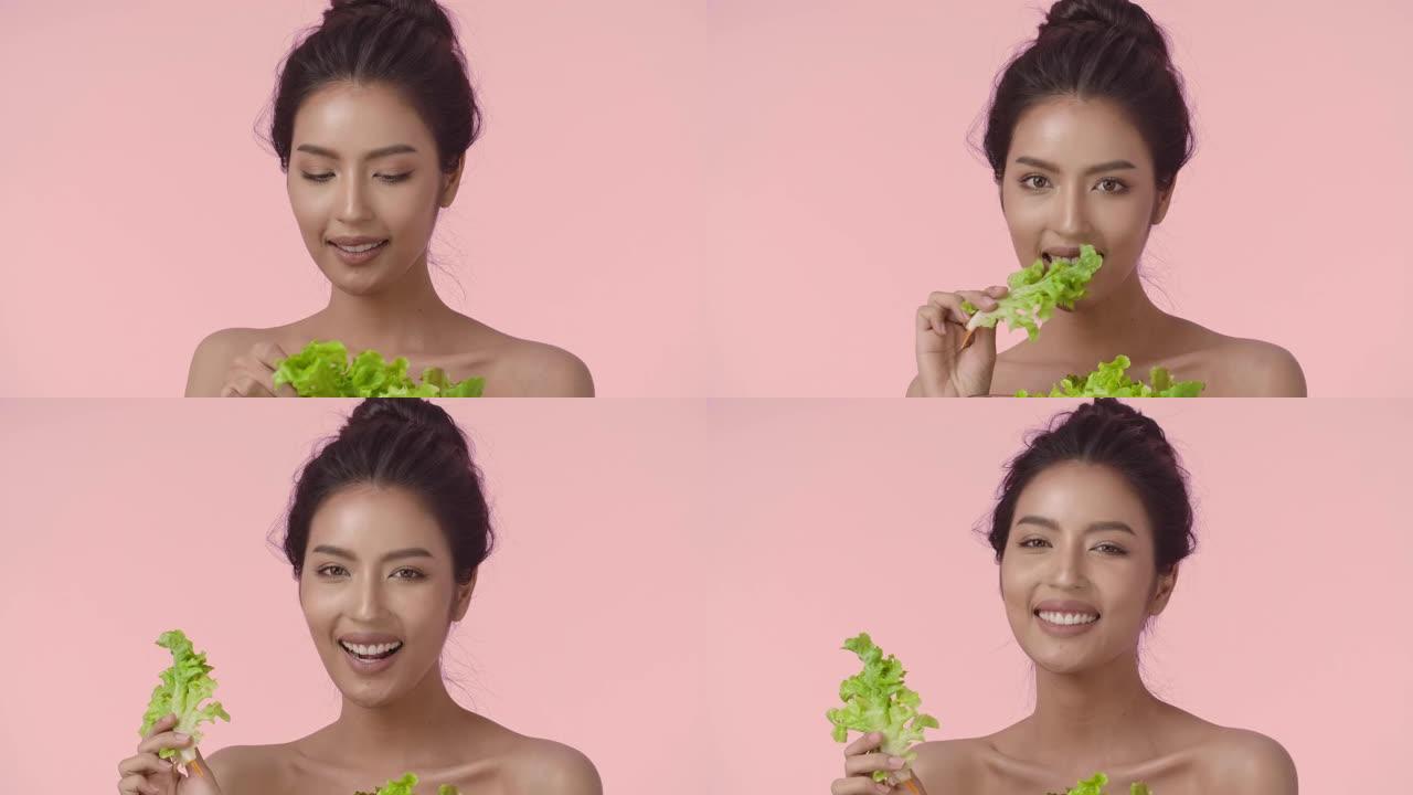 年轻亚洲女性的特写美女肖像，完美光滑健康的皮肤吃沙拉在粉红色的背景下。护肤商业概念。