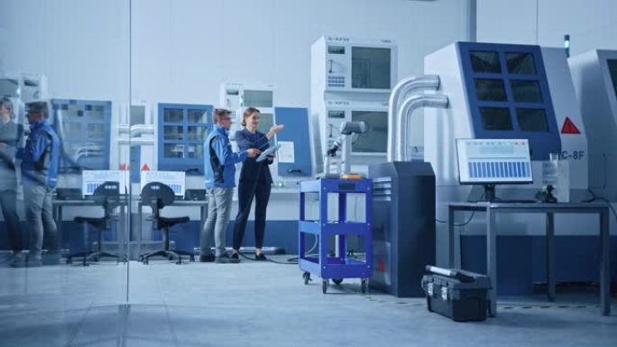 现代工厂: 女项目经理和男工程师站着，说话和使用平板电脑编程机器人手臂装配线。高科技数控机械的现代设