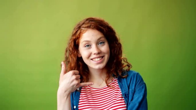 漂亮女孩的肖像显示叫我的手势和绿色背景上的微笑