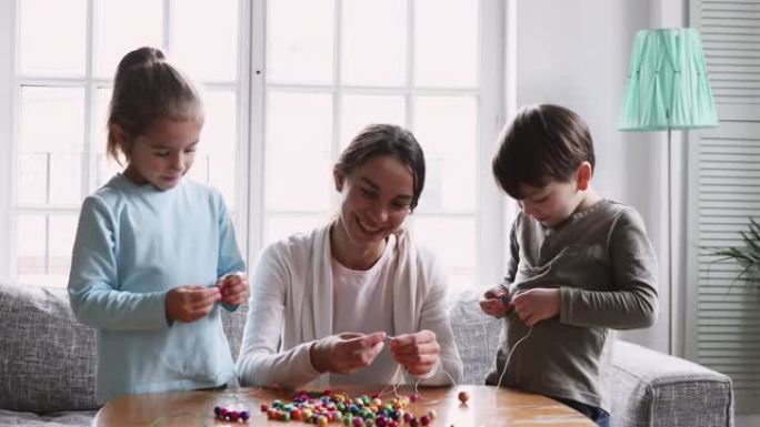 年轻的混血保姆教小孩子制作手工手镯。