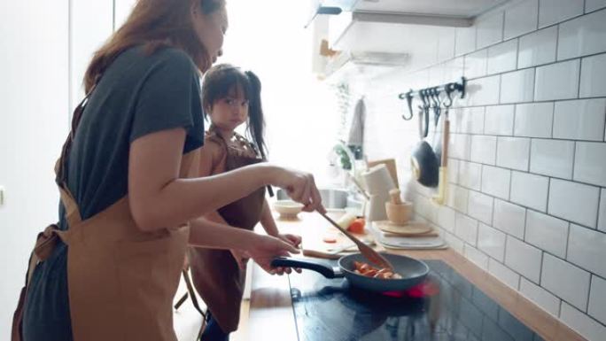 千禧一代的母亲用女儿的帮助手在家做饭煎蛋卷在厨房准备早餐。