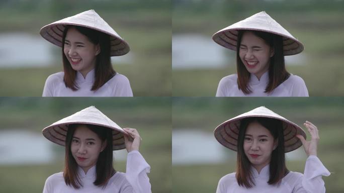 一位东南亚少年的美丽年轻女子穿着白色连衣裙，手持竹编帽子。心情愉快地站着对着镜头大笑