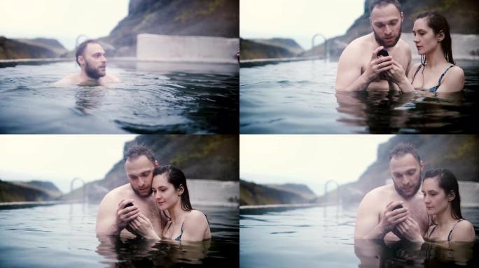 年轻美丽的夫妇在山谷的温泉里游泳，在冰岛一起用智能手机看照片。