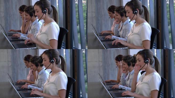 在呼叫中心工作的女性客户服务代表使用笔记本电脑接听电话和输入信息