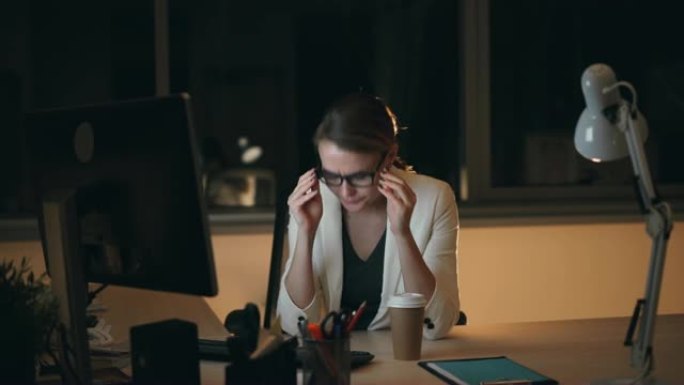穿着眼镜和西装的疲惫的金发女郎深夜在电脑上工作，喝外卖咖啡感到疲倦和疲惫。工作、过度劳累和喝酒的概念