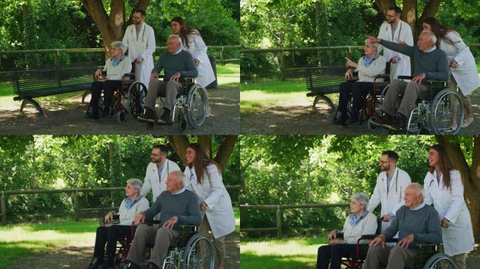 在阳光明媚的日子里，无忧无虑，快乐的社会工作者和坐在轮椅上的老年夫妇在绿色公园散步