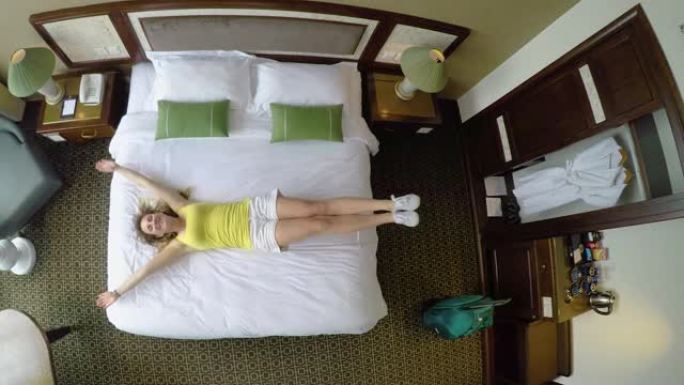 自上而下: 放松假期的年轻女子跳到酒店房间的床上。