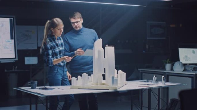 在创意建筑局，两名专业工程师在市区模型上工作。城市规划者致力于功能性建筑模型。他们交谈并使用数字平板