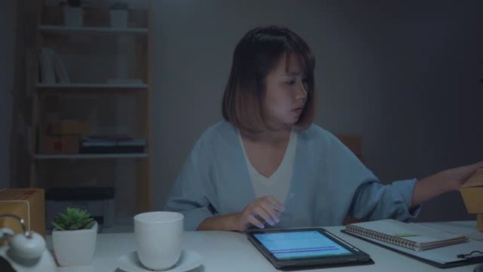 亚洲年轻企业家商业女性中小企业在线检查库存产品，保存到平板电脑，在家深夜工作喝咖啡。家庭办公室概念的