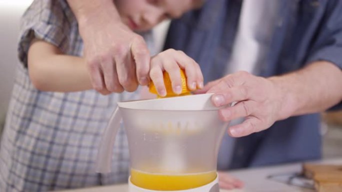 父亲帮助男孩制作新鲜的橙汁