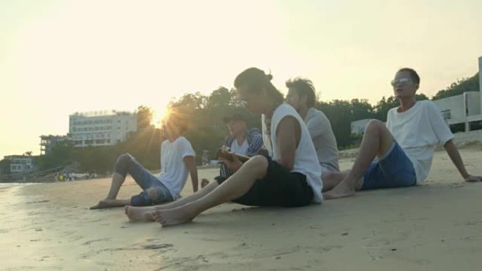 五名年轻的亚洲成年男子坐在沙滩上放松唱歌弹吉他