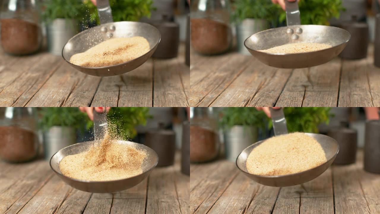 慢动作: 女厨师将面包屑放在热锅中混合时，面包屑落在桌子上。