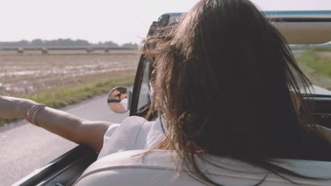 SLO MO-TIME翘曲效果无忧无虑的年轻女子沿着阳光明媚的乡村道路驾驶敞篷车