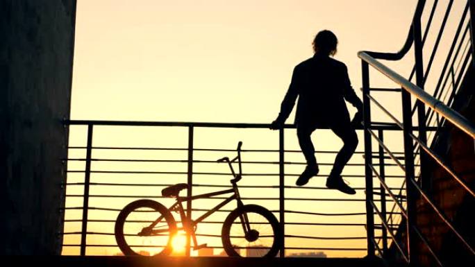 楼梯栏杆上坐着一个男性青少年，他的自行车在他旁边