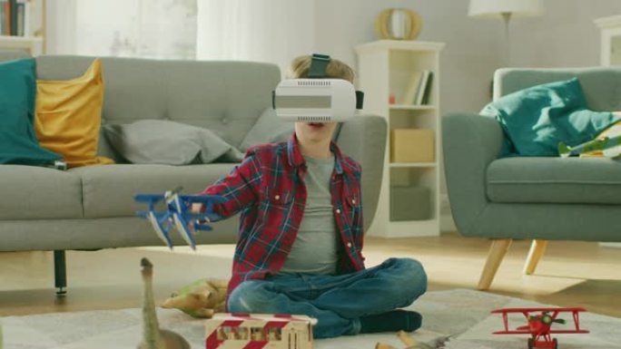 戴着虚拟现实耳机的聪明小男孩坐在客厅的地毯上玩玩具飞机。快乐的孩子在家里使用未来的AR眼镜。