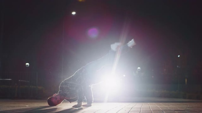 年轻的霹雳舞的慢动作很有趣，晚上在城市停车场用车灯跳舞
