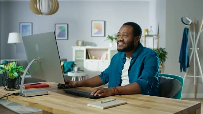 微笑的年轻人出现在他的办公桌前，开始在个人电脑上工作。背景舒适的客厅。