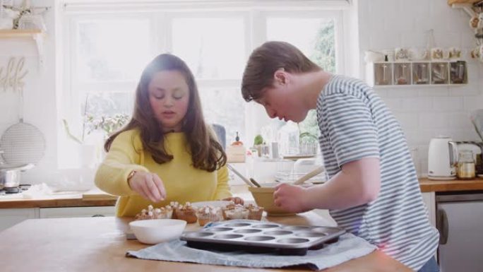 年轻的唐斯综合症夫妇在家里的厨房里用棉花糖装饰自制纸杯蛋糕