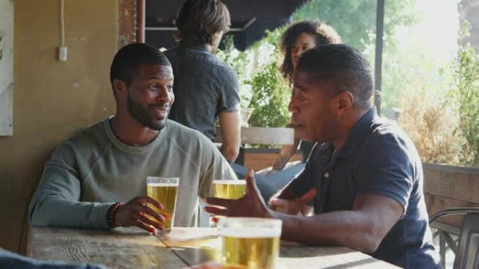 两个男性朋友在比赛前在体育酒吧户外聚会，享受饮料