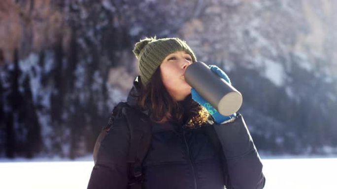 女孩从水瓶中喝淡水来解渴，并为背景降温雪山和松林。山的纯净水。