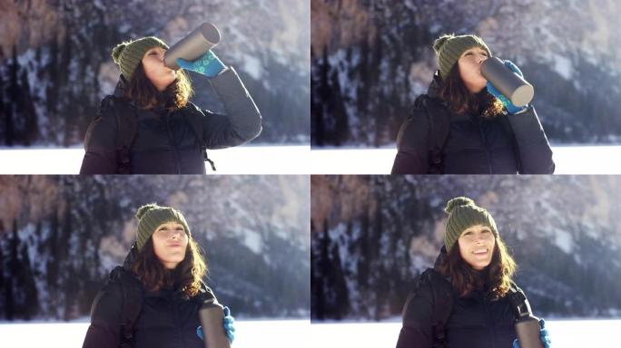 女孩从水瓶中喝淡水来解渴，并为背景降温雪山和松林。山的纯净水。
