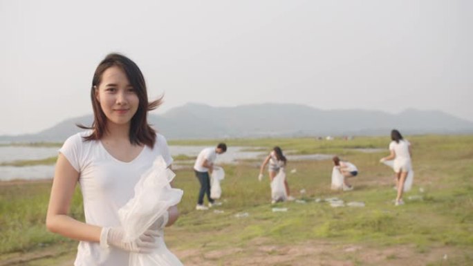 年轻的亚洲女士志愿者的肖像有助于保持大自然的清洁，看着相机，并在海滩上带着白色垃圾袋微笑。