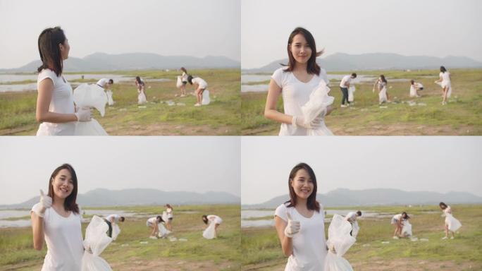 年轻的亚洲女士志愿者的肖像有助于保持大自然的清洁，看着相机，并在海滩上带着白色垃圾袋微笑。