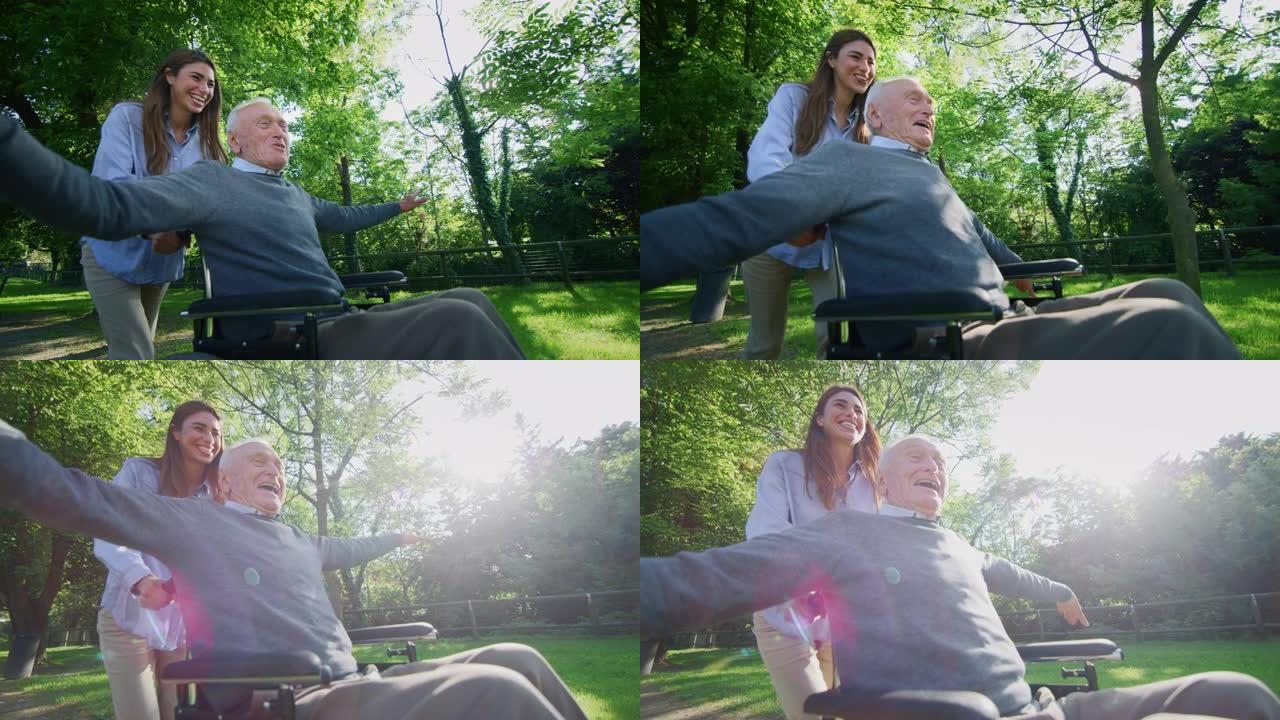 坐在轮椅上的无忧无虑快乐的孙女和祖父的慢动作在阳光明媚的日子里在绿色公园里跑步