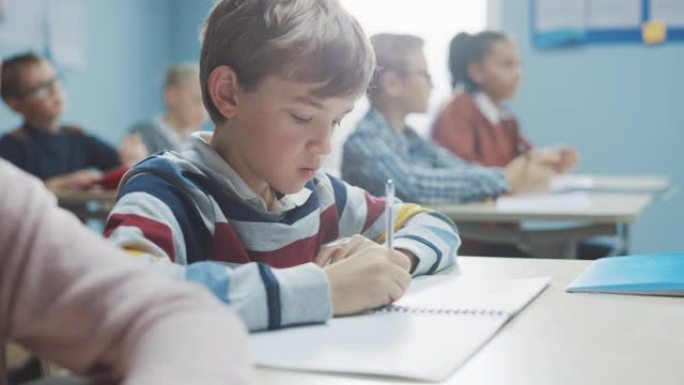 在小学课堂上: 才华横溢的高加索男孩的肖像在练习笔记本上写作，参加考试和写作考试。多元化的聪明孩子勤