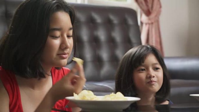 两姐妹亚洲少女在家享受吃薯片