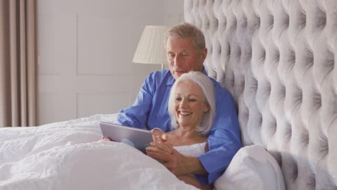 在Covid 19锁定期间，在家中的高级夫妇在床上使用数字平板电脑进行自我隔离