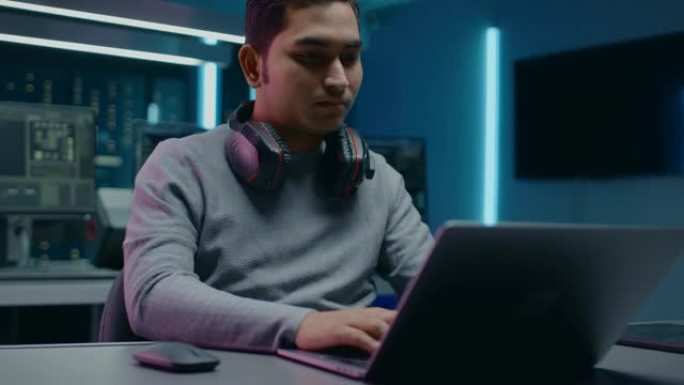 软件开发人员/黑客/程序员坐在他的办公桌前，在背景黑暗霓虹灯高科技环境中工作的笔记本电脑，有多个显示