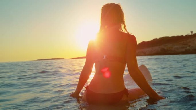 特写: 无法辨认的健康女人坐在冲浪板上，看着日落