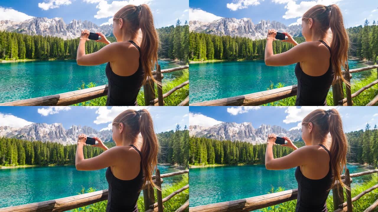 探索多洛米蒂山腰的女游客，站在特伦蒂诺的卡雷扎湖边，背景是拉特马尔山脉，用智能手机拍照