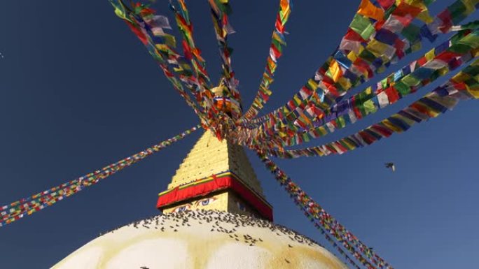 尼泊尔加德满都Boudhanath佛塔周围的彩旗。许多鸟坐在底部。蓝天白月亮。UHD