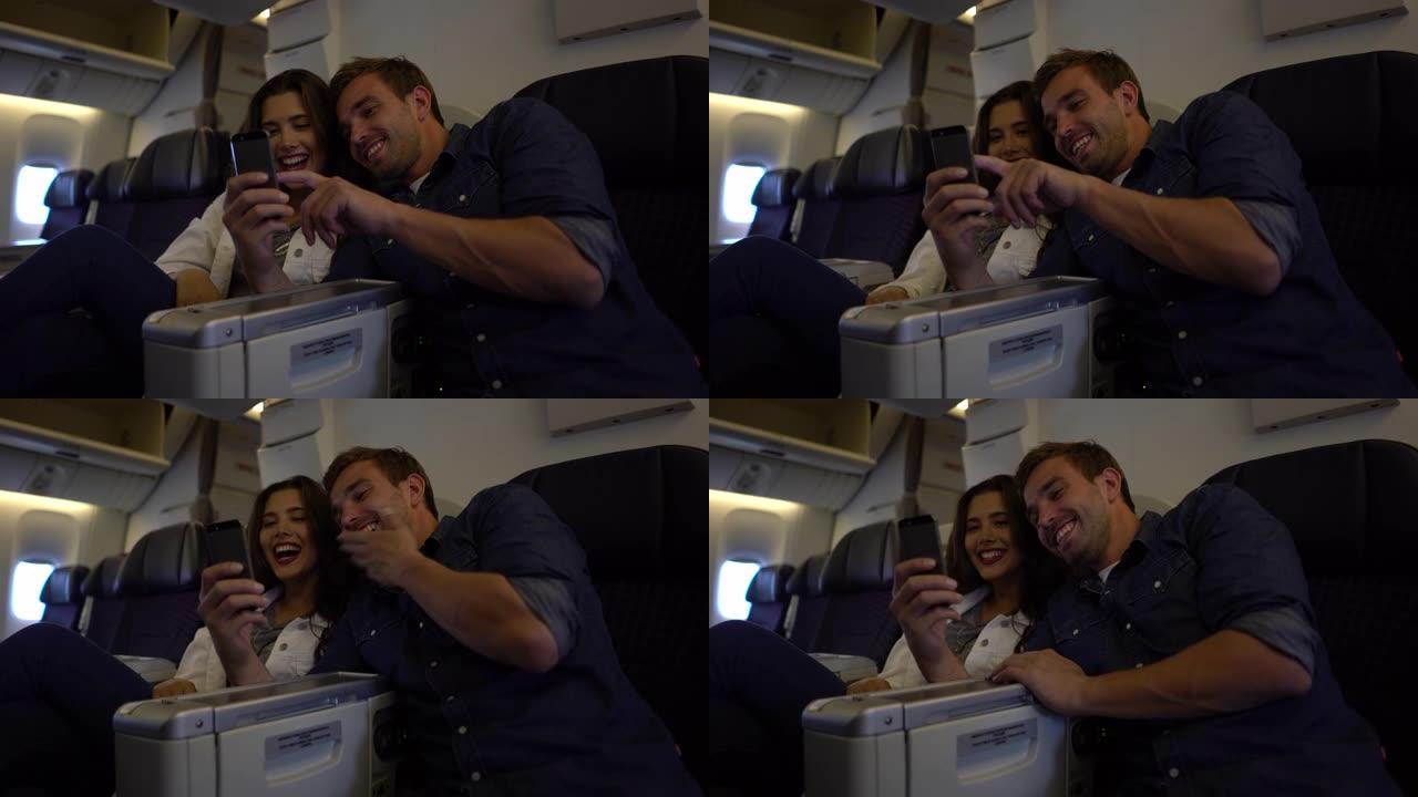 快乐的年轻夫妇乘飞机旅行，一边聊天一边看智能手机