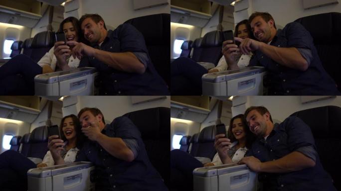 快乐的年轻夫妇乘飞机旅行，一边聊天一边看智能手机