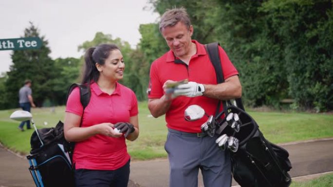 成熟的夫妇打高尔夫球，背着高尔夫球袋，看着记分卡