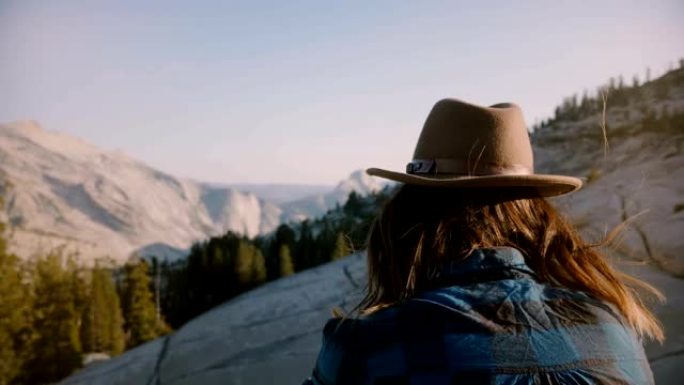年轻的旅游女孩独自坐在一块岩石上，在优胜美地国家公园观看美丽的山景。