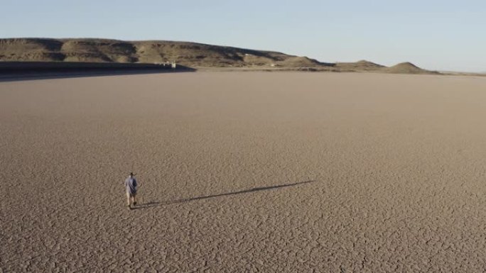 由于气候变化和全球变暖造成的干旱，一个饱受摧残的农民走过干燥大坝的破裂的泥面的4k高鸟瞰图