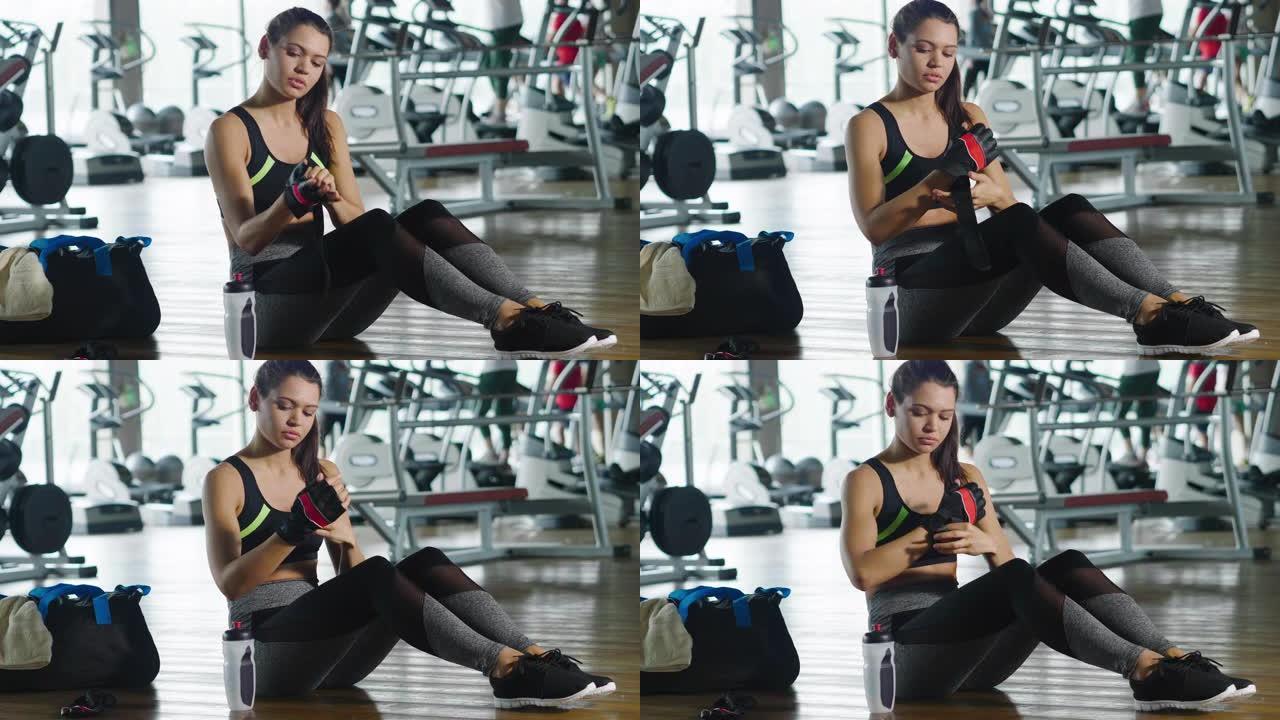 坐在健身房地板上的健康女人用一瓶能量饮料固定鞋子