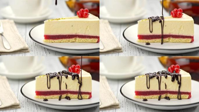红醋栗芝士蛋糕放在盘子上，上面装饰着红色浆果，上面倒入巧克力釉。背景中模糊的白杯茶和茶壶。滑块镜头，