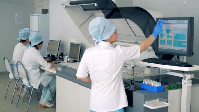 女实验室专家正在一家制药厂的触摸屏上操纵生化分析仪。